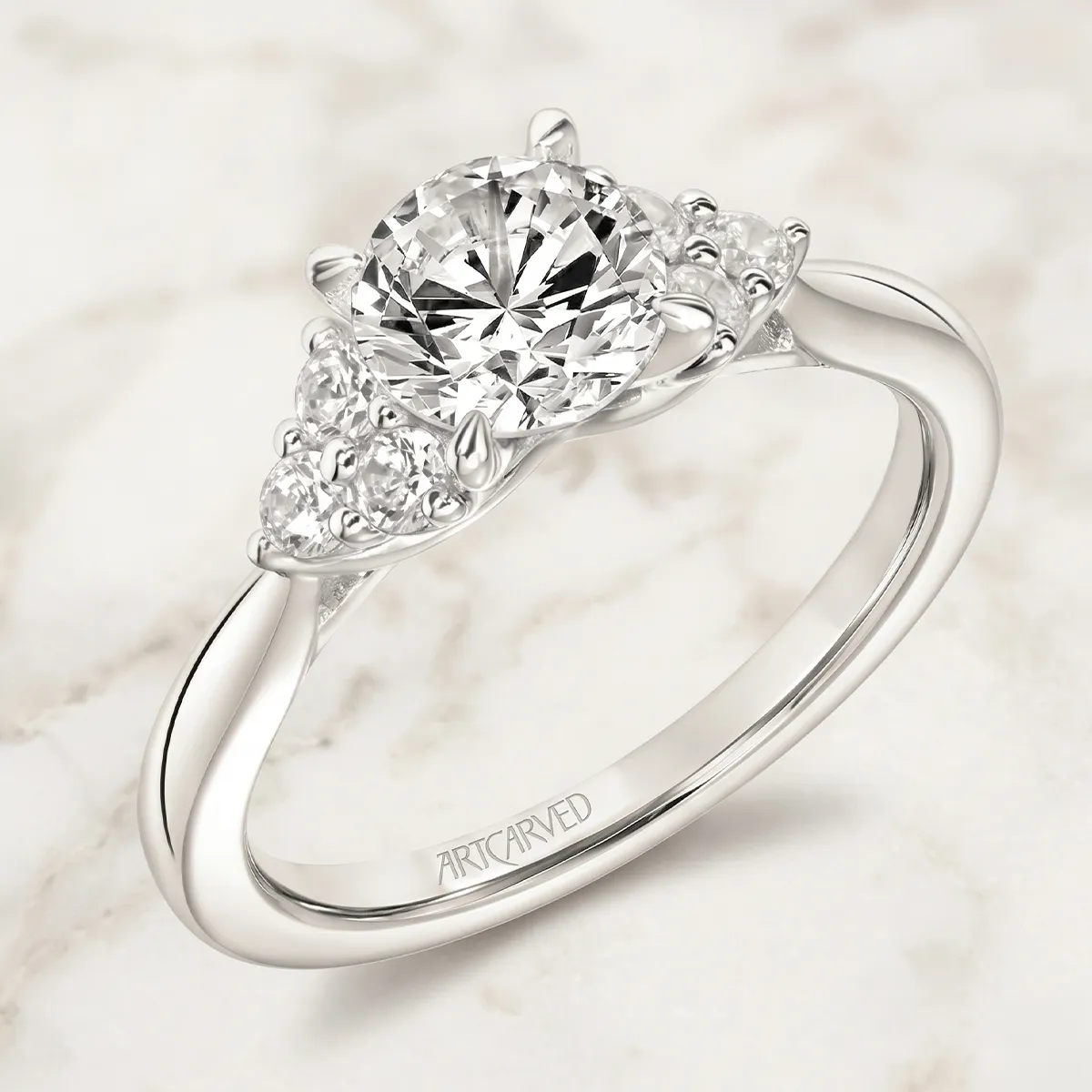 Elegant diamond engagement ring with round center stone and side accents on a marble background.