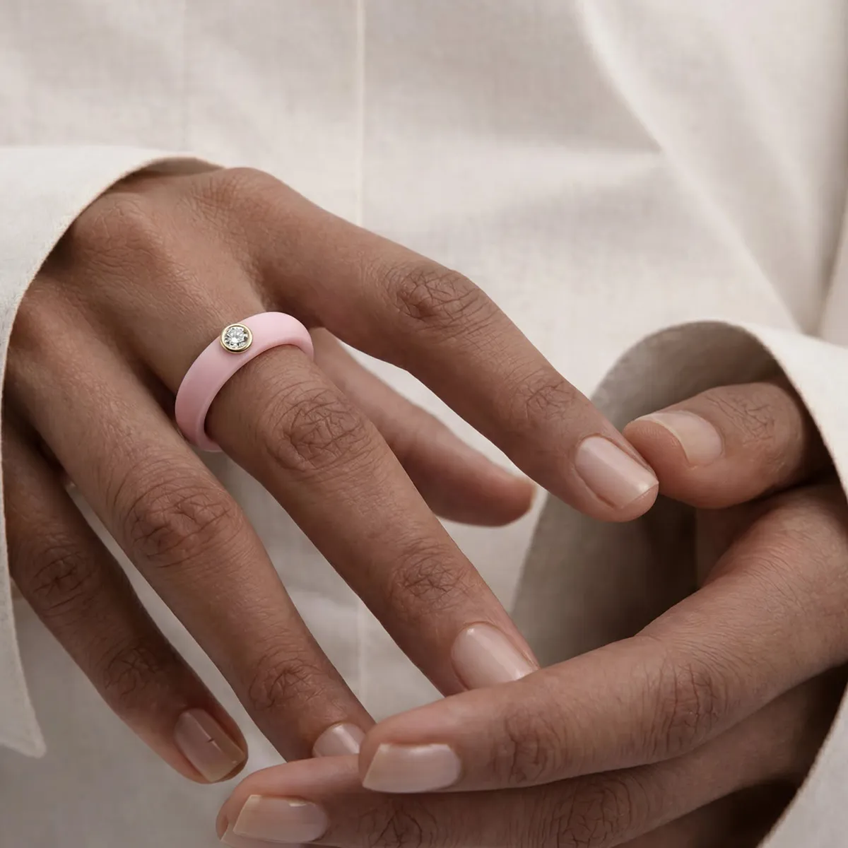Hand wearing a pink ring with a diamond on the ring finger.
