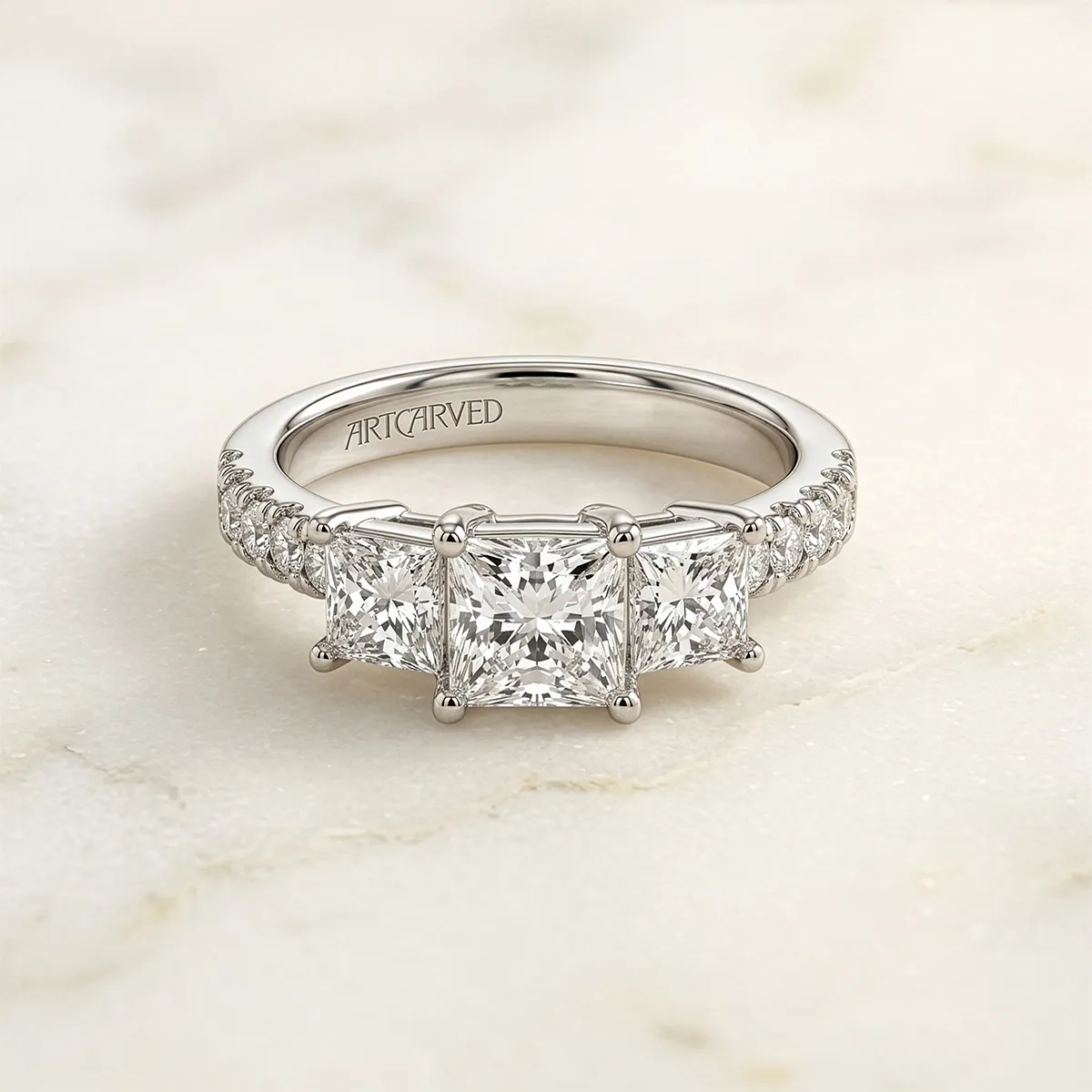 Diamond engagement ring with three square diamonds on a marble surface.
