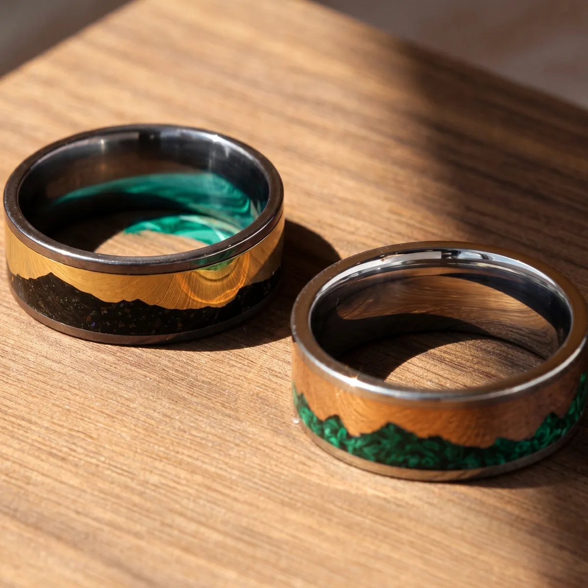 Two rings with wood and green inlay on a wooden surface, showcasing unique designs.