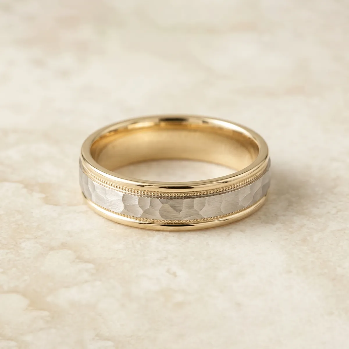 Gold and silver men's wedding band with textured design on a light background.