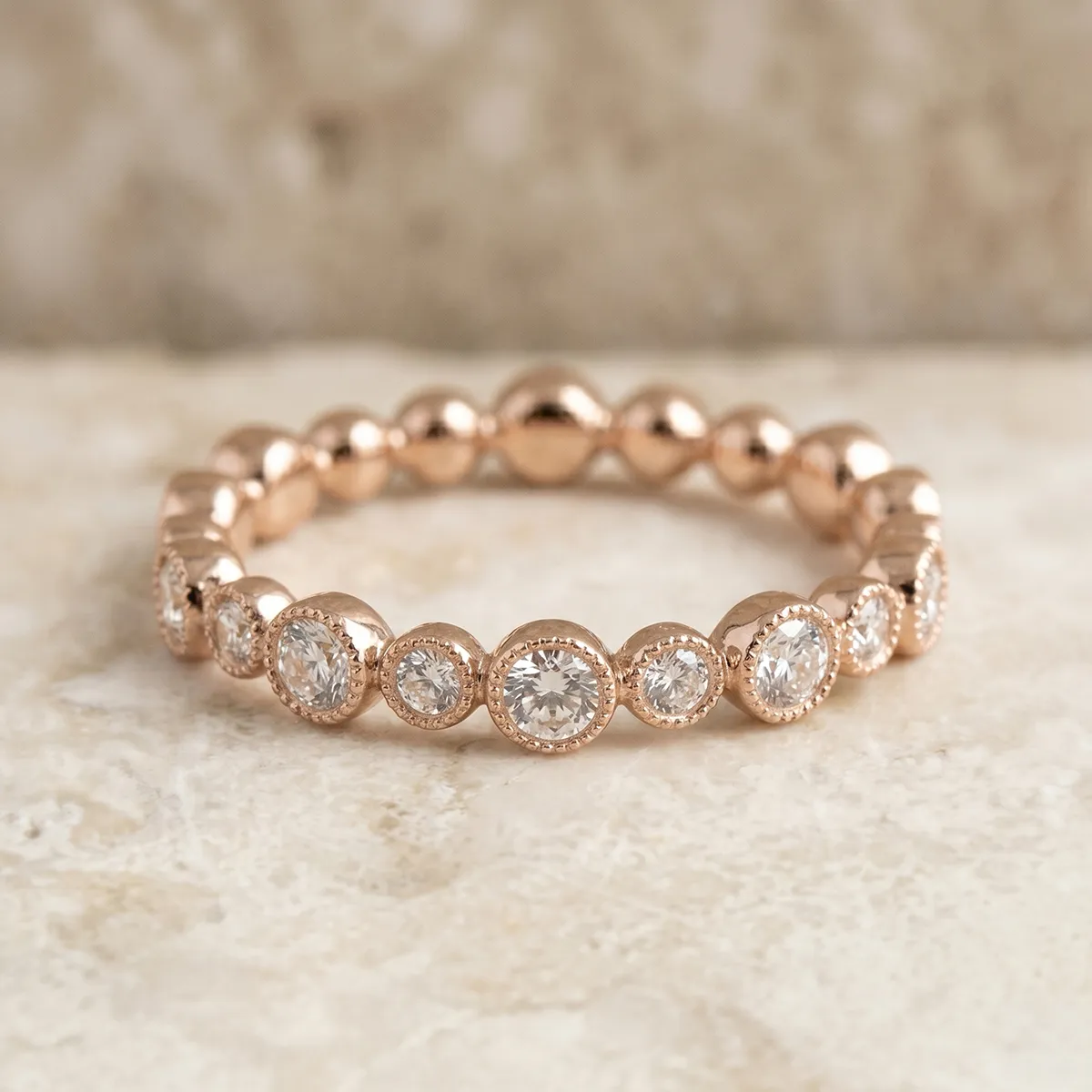 Rose gold diamond eternity band on a marble surface. Explore women's wedding bands at Pearce Jewelers.