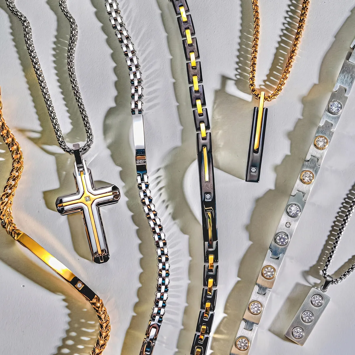 Men's necklaces with cross and bar pendants in gold and silver tones on a white background.