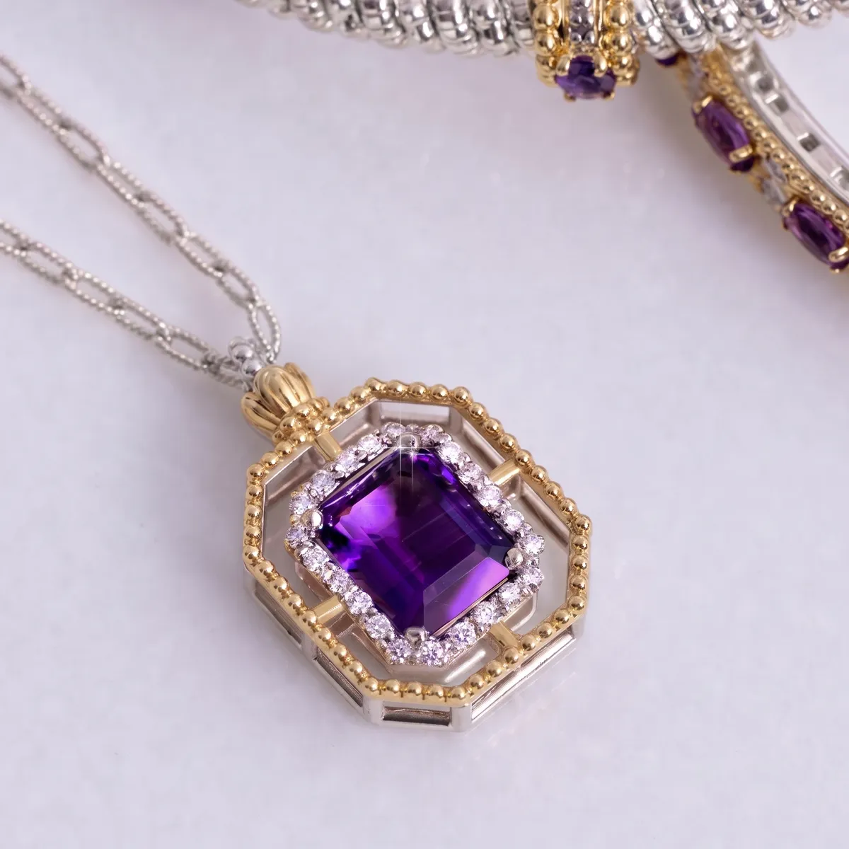 A gold and silver pendant with a purple gemstone and diamond accents on a chain.