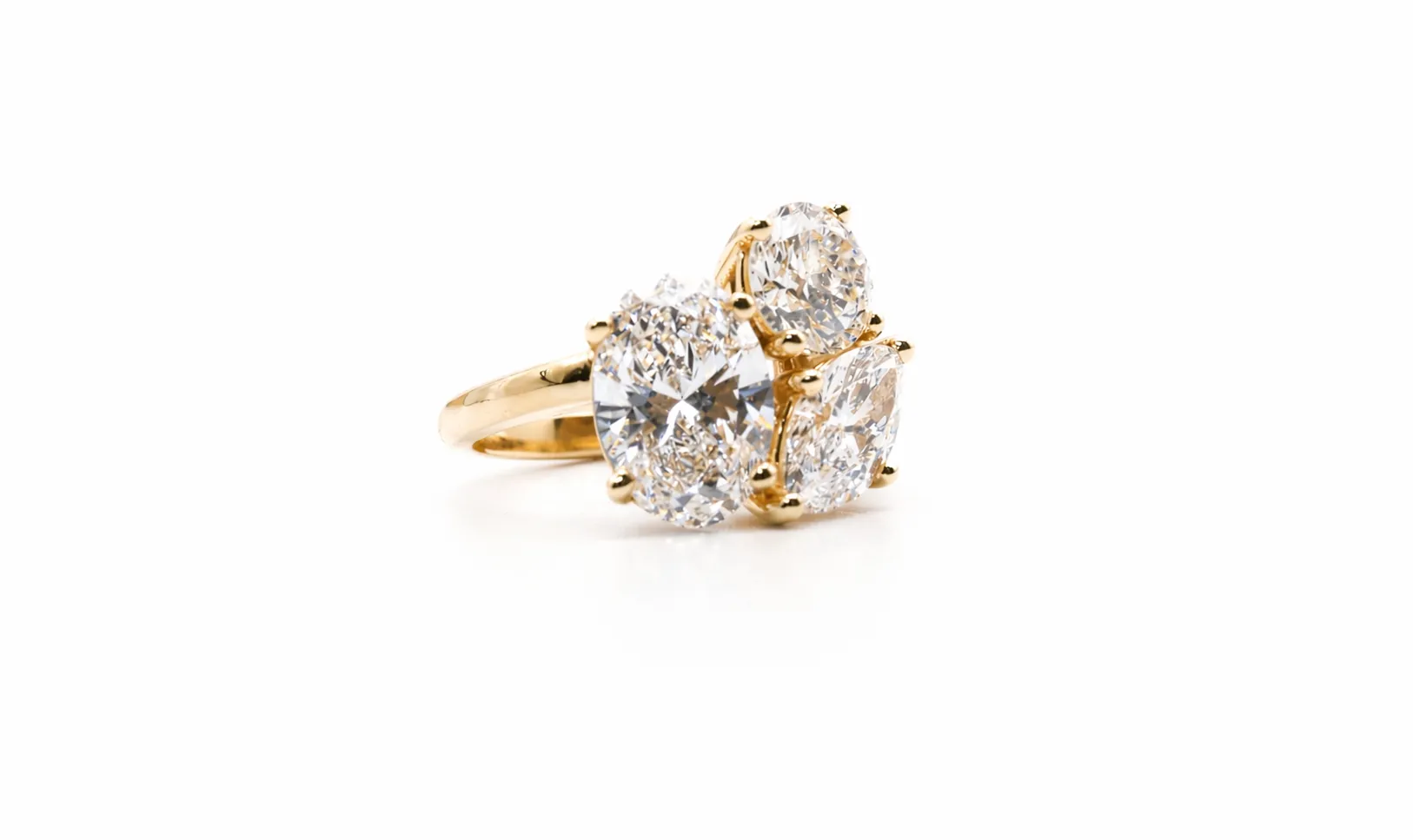 A gold ring with three large, sparkling diamonds set in a cluster design on a white background.
