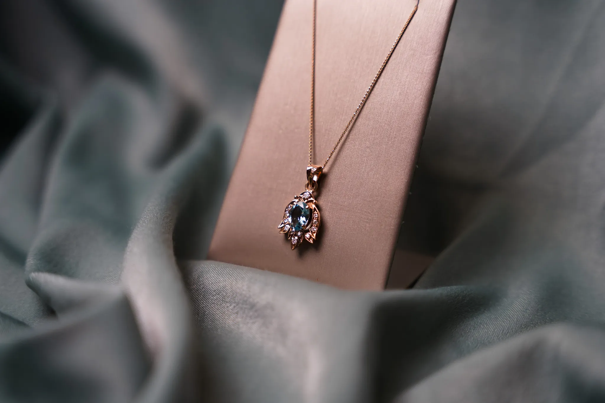 Elegant vintage gold chain necklace with blue gemstone and diamond pendant displayed on velvet backdrop.