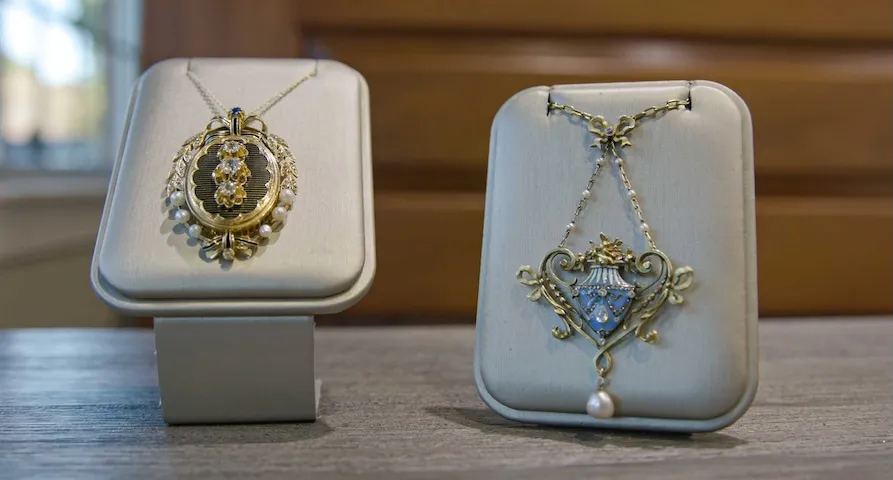Two ornate necklaces displayed on stands, featuring intricate designs and pearls.