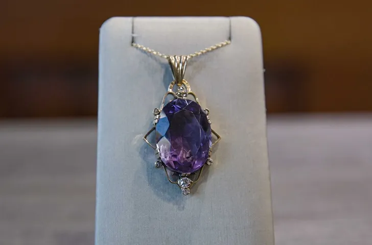 A gold necklace with a large purple gemstone pendant displayed on a stand.