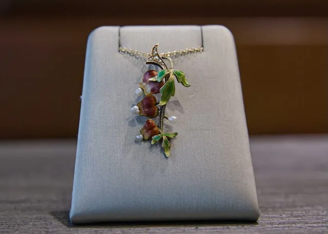 A floral pendant necklace with pearls displayed on a gray stand.