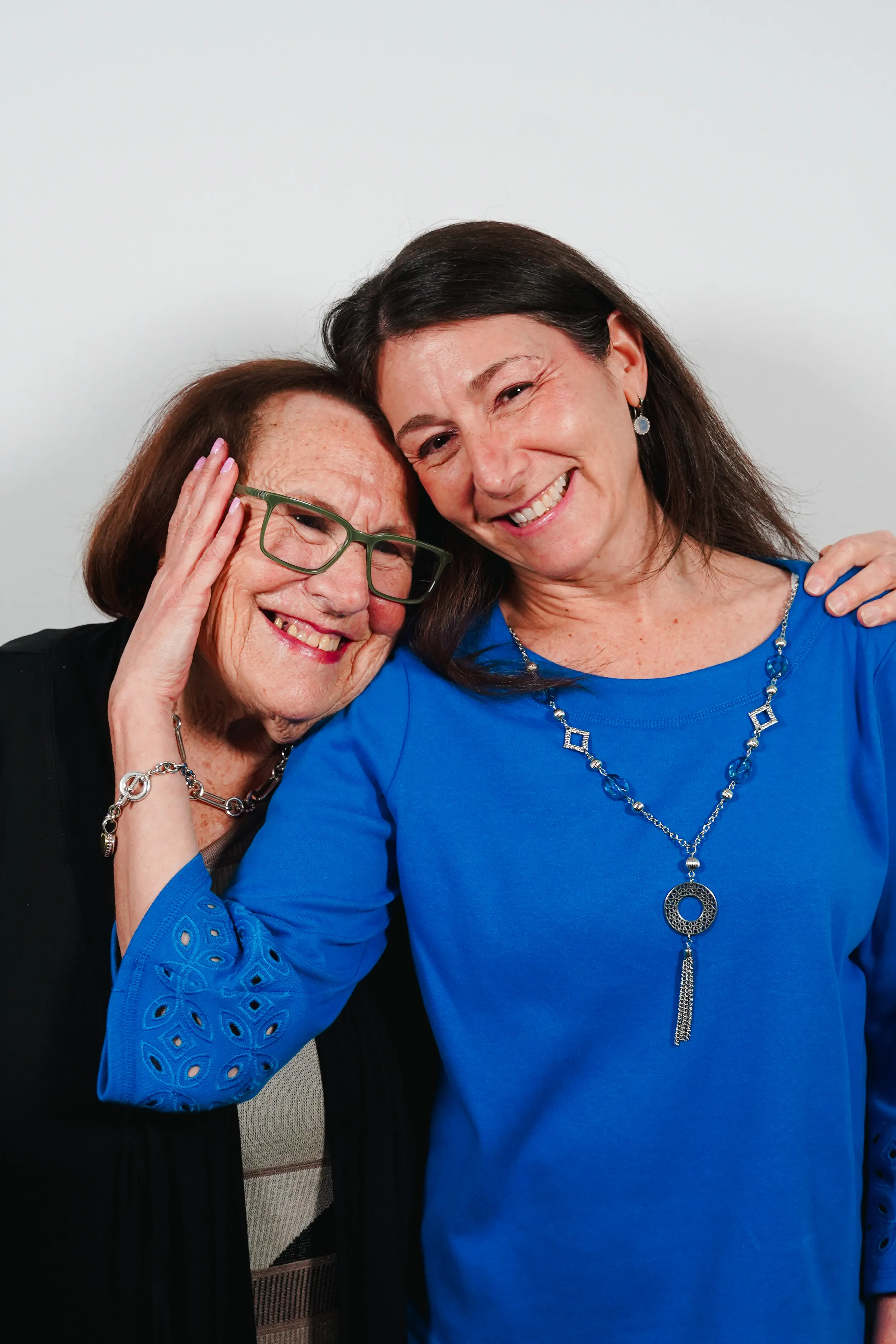 Two women smiling, embracing each other closely, one wearing glasses and the other in a blue top.
