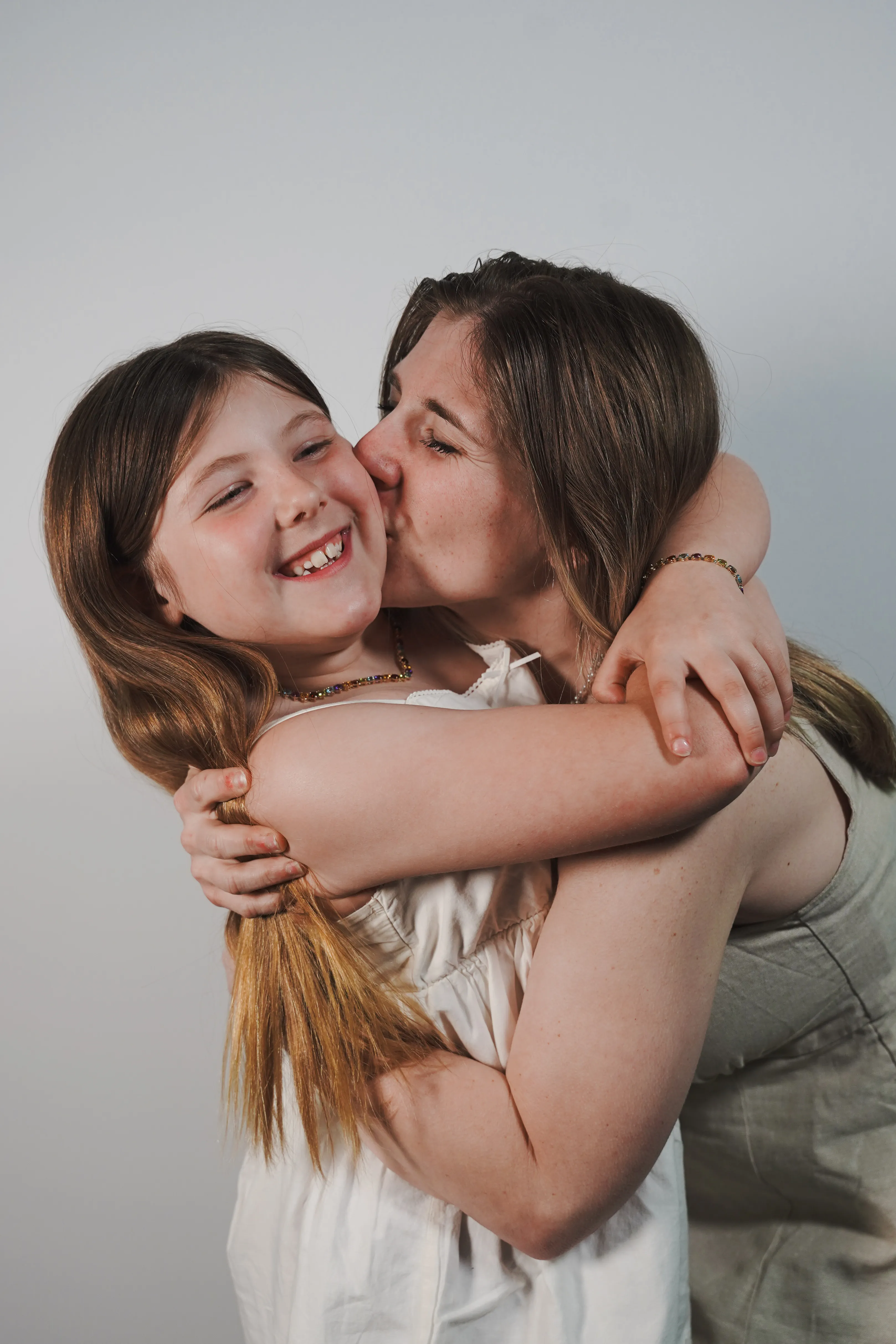 A woman kisses a smiling girl on the cheek, both embracing warmly.