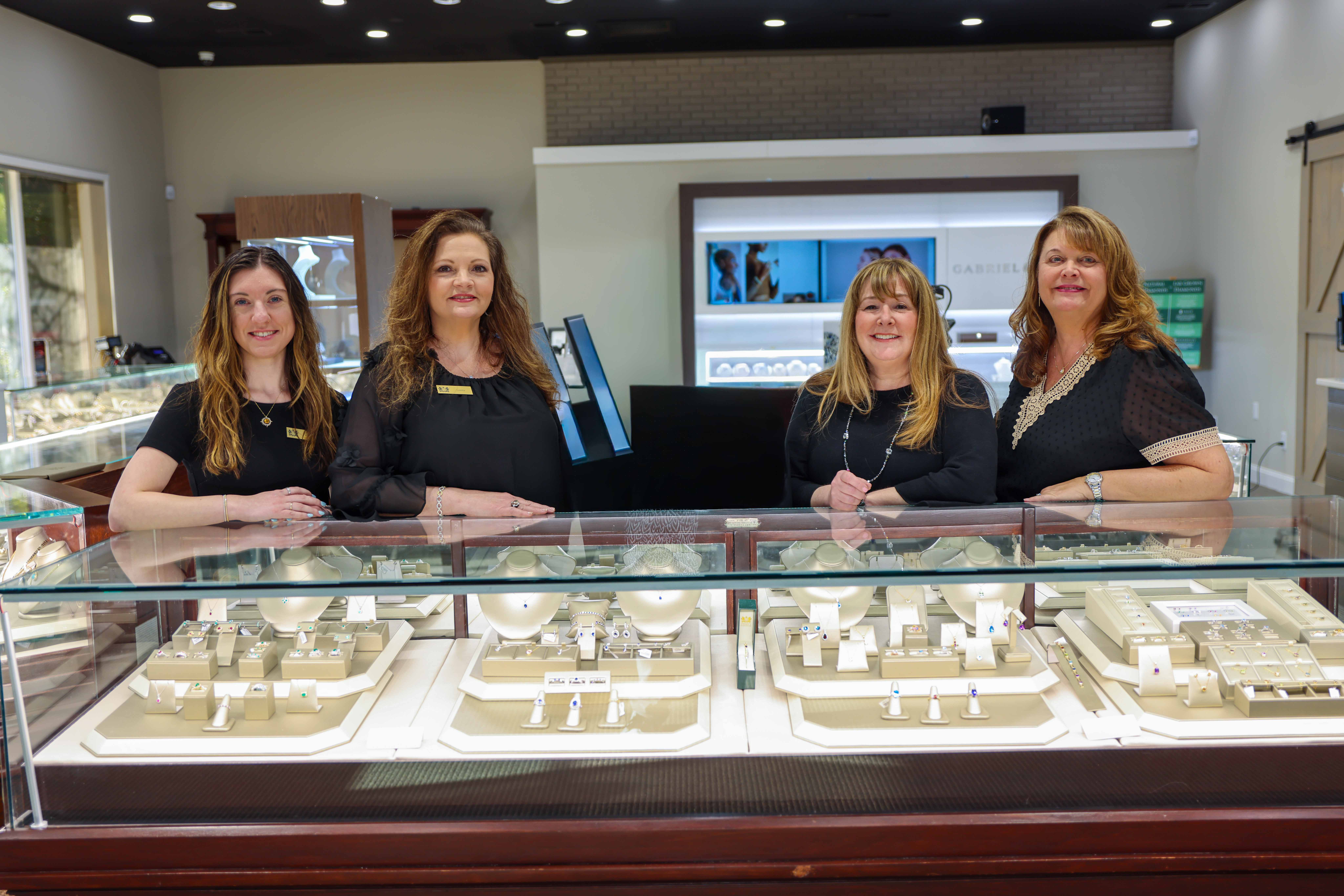Perry's Emporium team members pose in front of jewelry displays, showcasing fine jewelry and engagement rings.