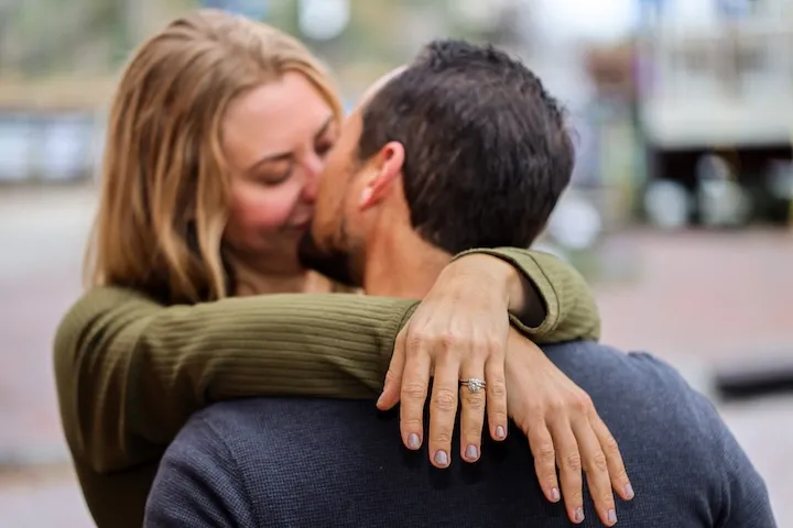A couple kissing, with the woman embracing the man, showcasing an engagement ring.