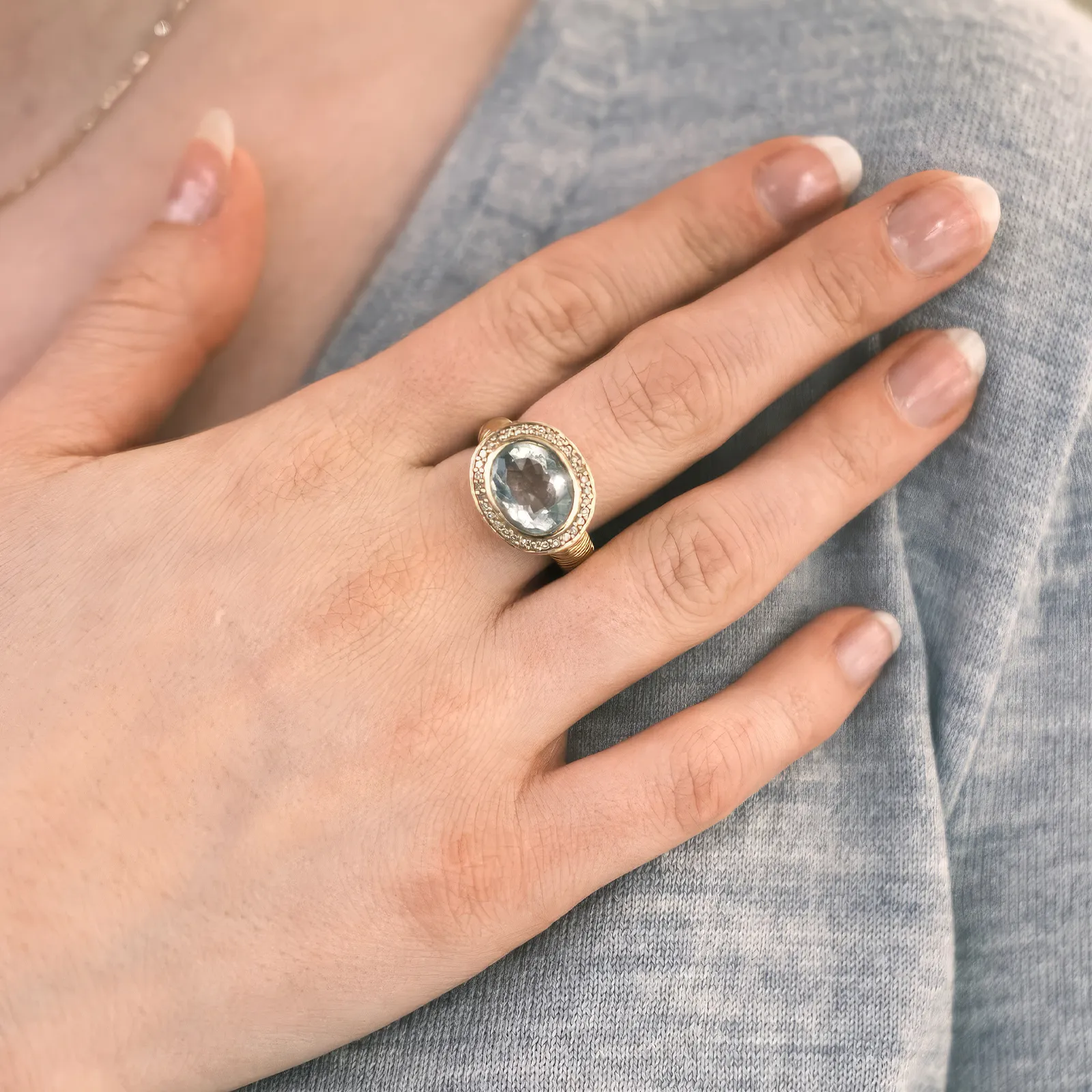 A hand wearing a gold ring with a large oval gemstone and a halo of smaller stones.
