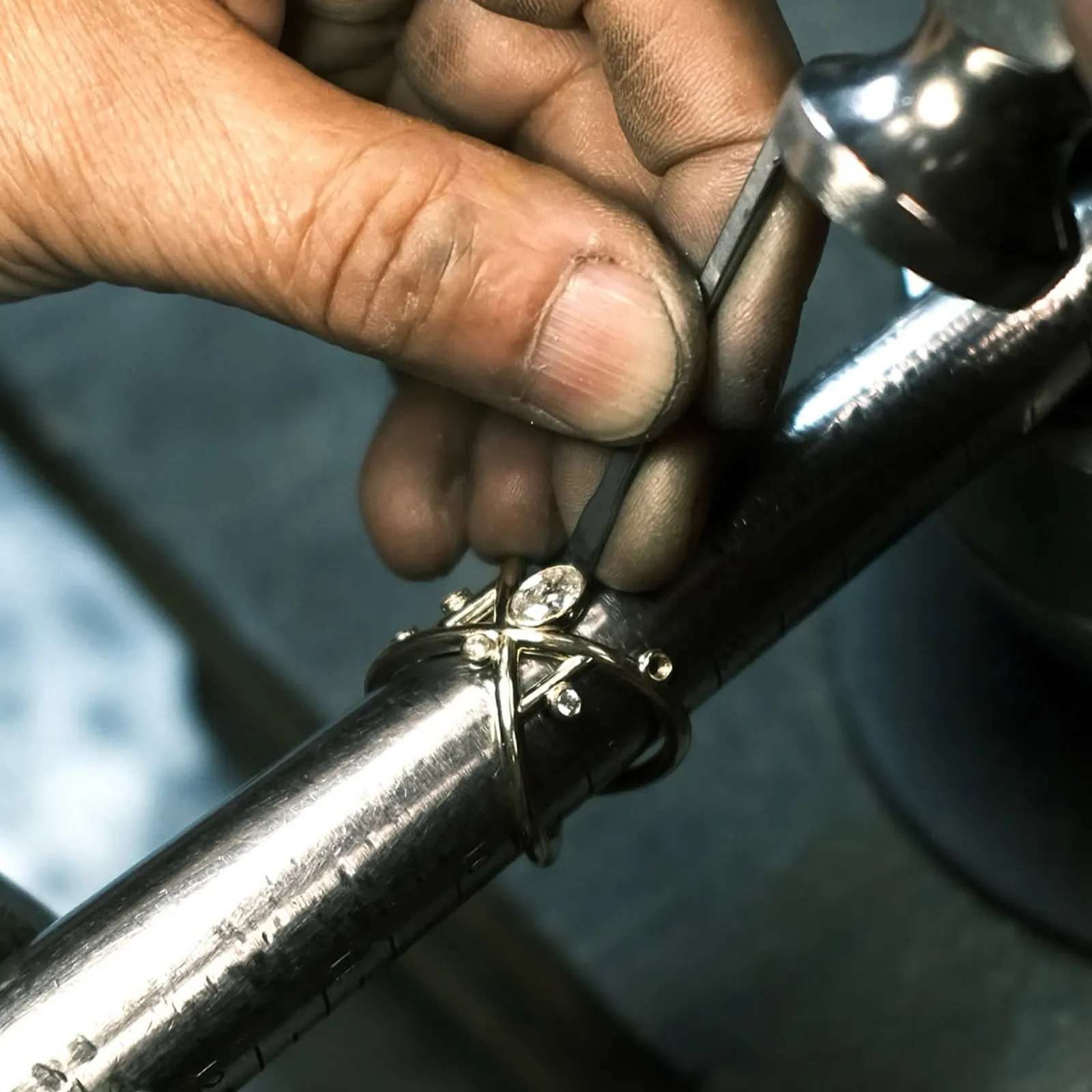 A jeweler's hand working on a ring with a tool on a metal mandrel.