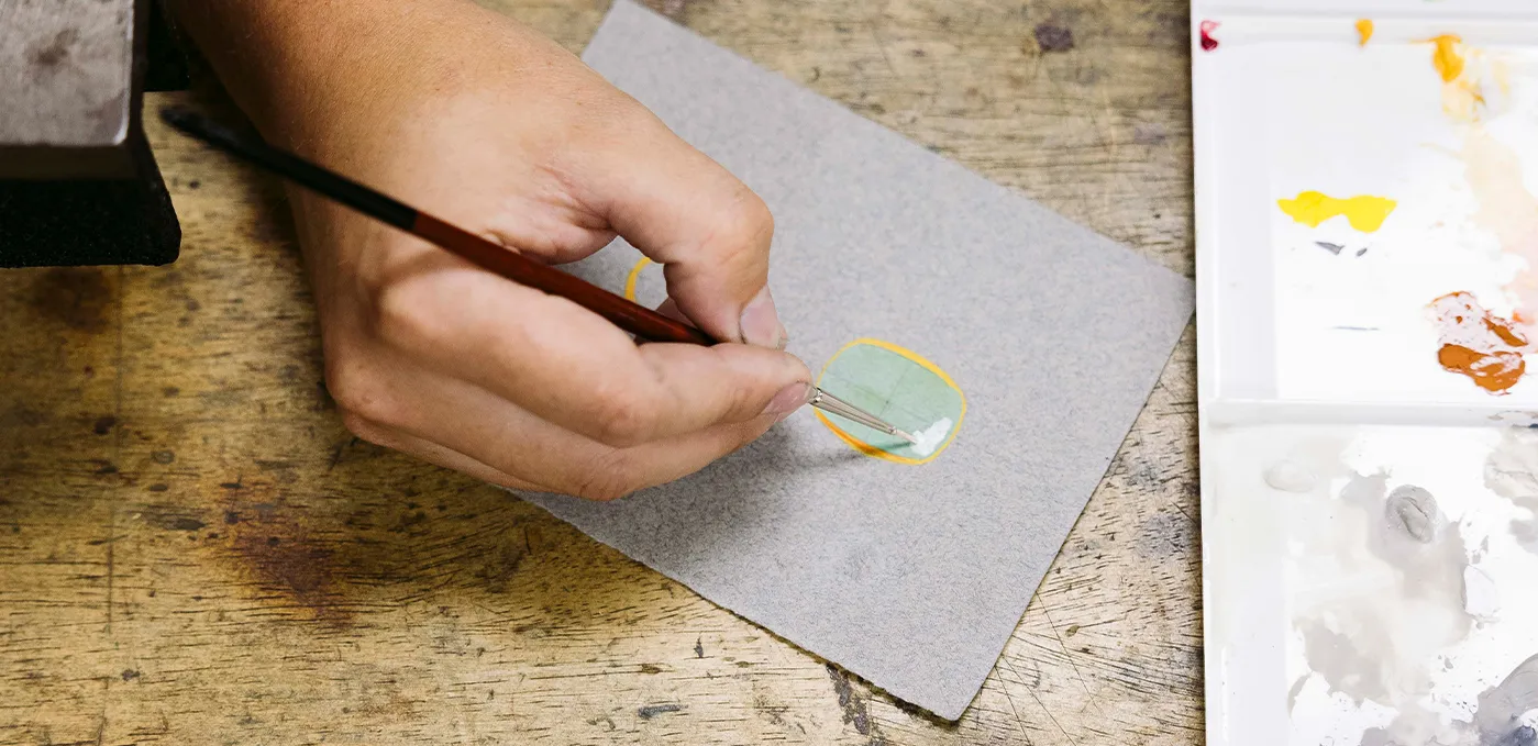 Hand painting on paper with a brush, palette with paint nearby.