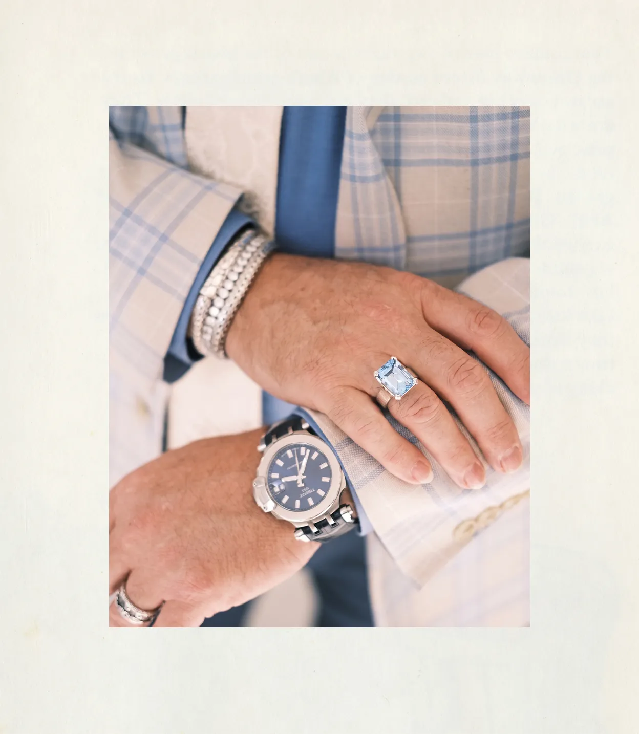 Man wearing a plaid suit with a large blue gemstone ring, silver watch, and bracelets.
