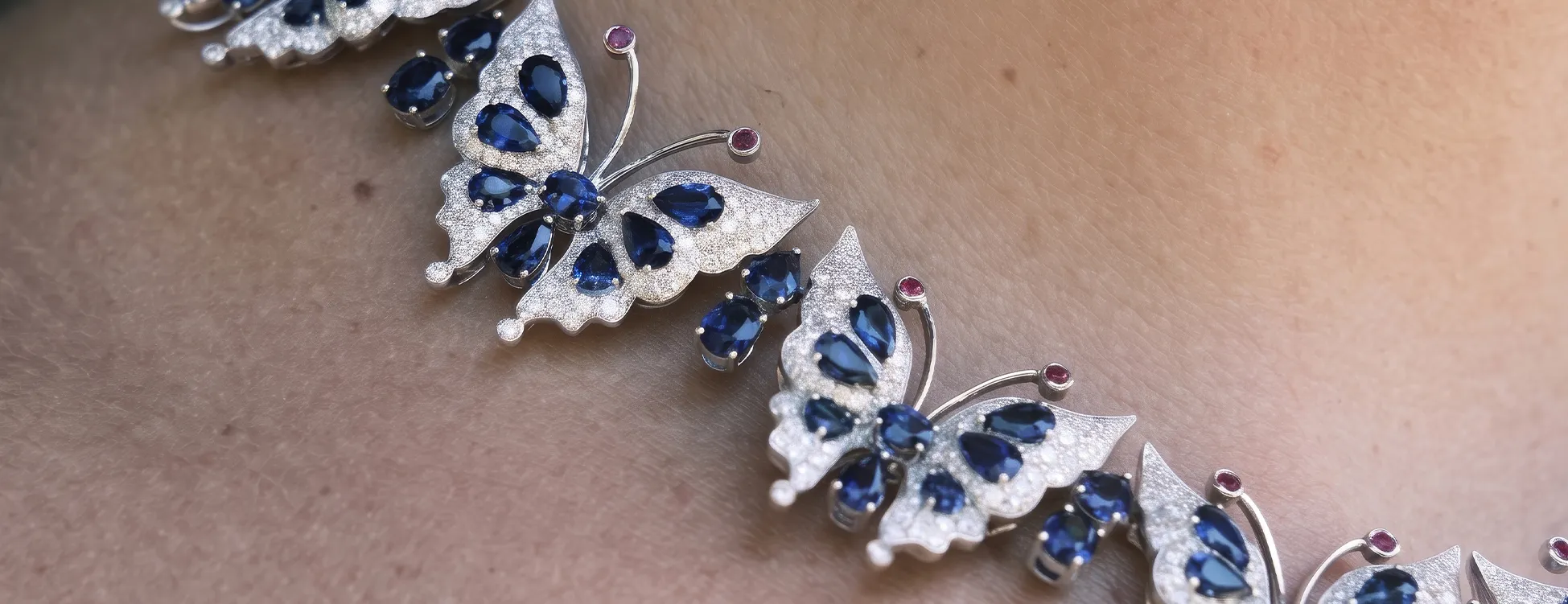 A necklace with butterfly designs featuring blue gemstones and small pink accents.