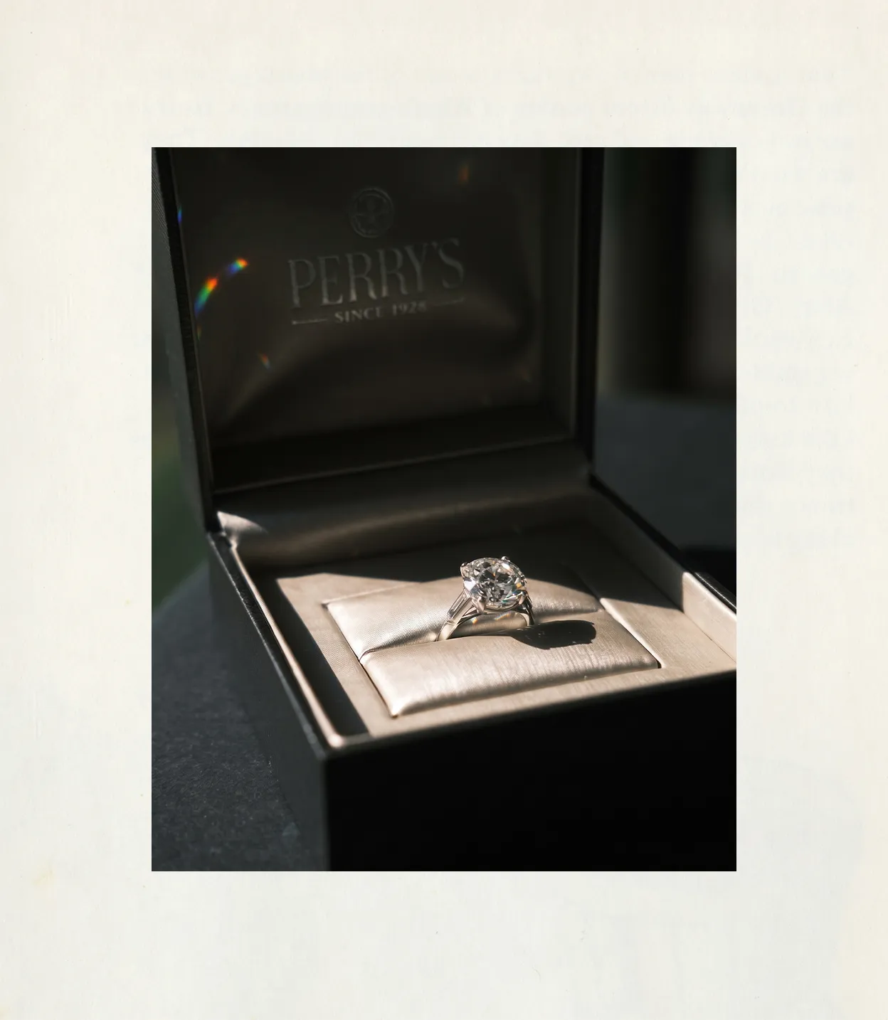 A diamond ring in a Perry's jewelry box, illuminated by soft light.
