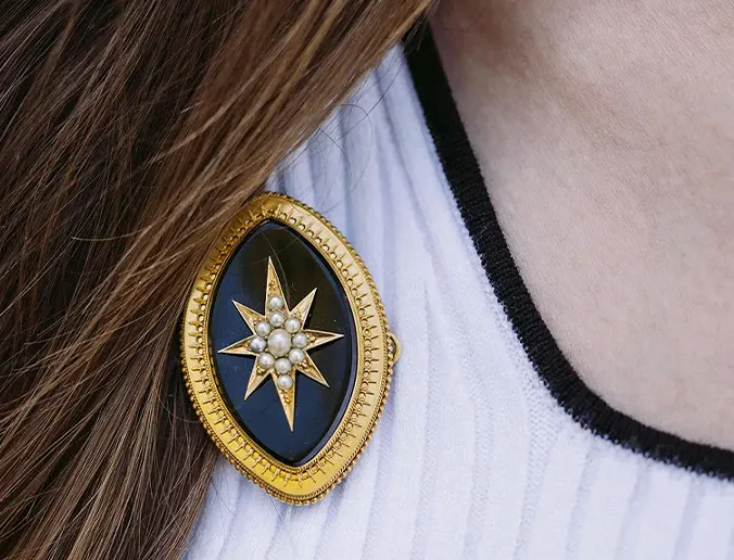 Antique enamel star brooch with pearls on a white and black garment.