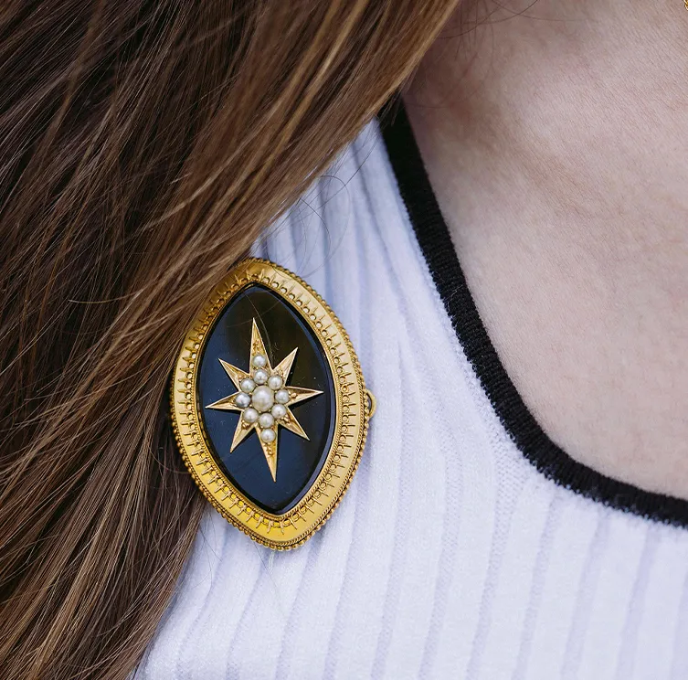 Antique enamel star brooch with pearls on a white and black garment.
