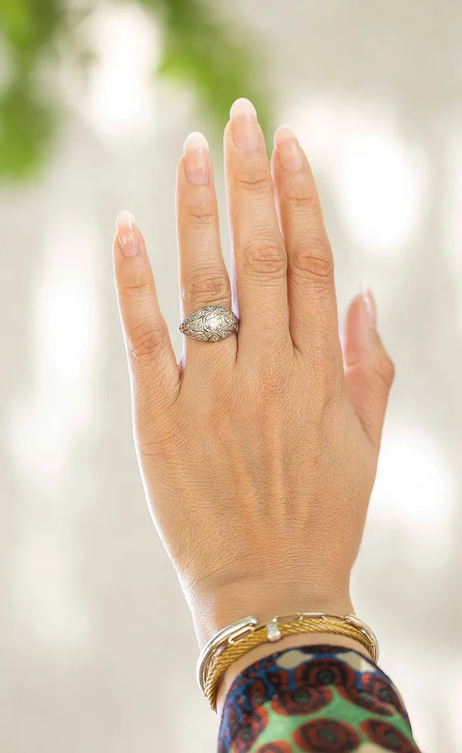 Hand wearing an ornate diamond ring and gold bangles, with a blurred background.