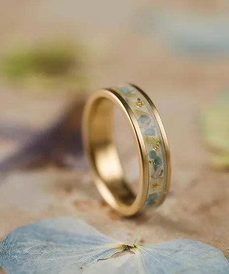 Gold ring with blue and gold inlay resting on hydrangea petals.