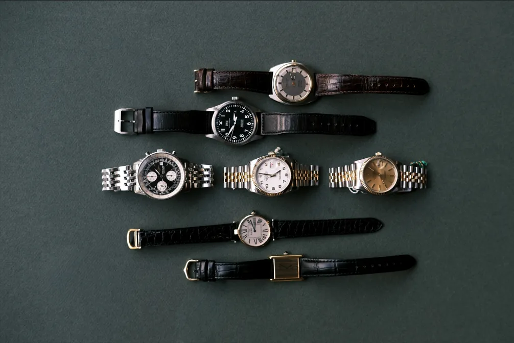 Seven pre-owned luxury watches from Perry’s on green felt, including two-tone dress watches, a pilot watch, a chronograph and gold dress watches