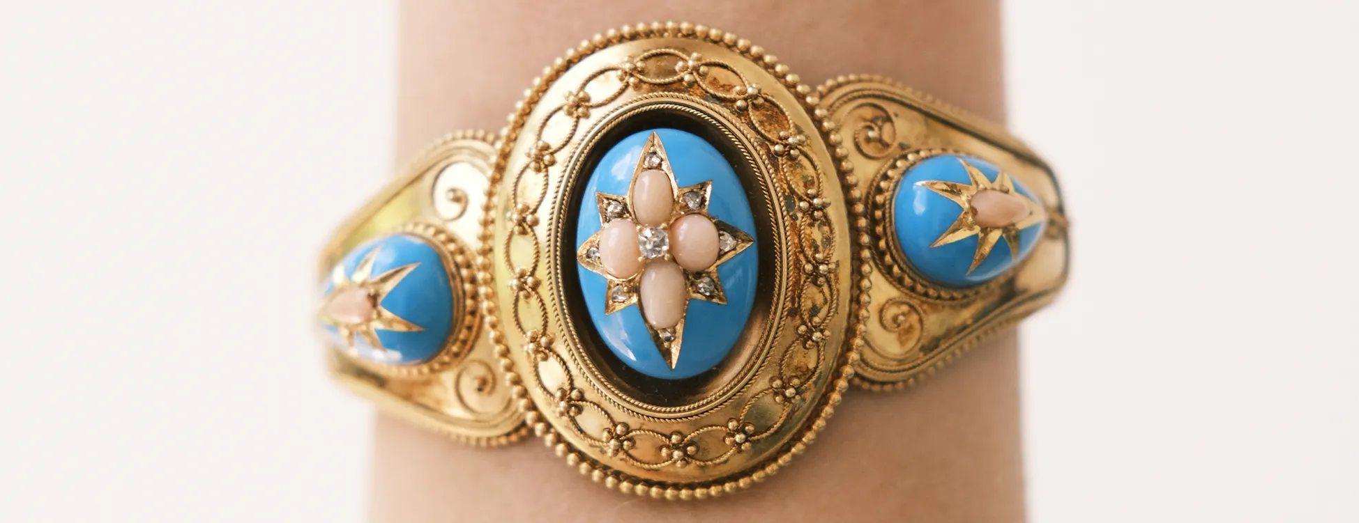 An ornate gold bracelet with blue enamel and pearl accents on a wrist.
