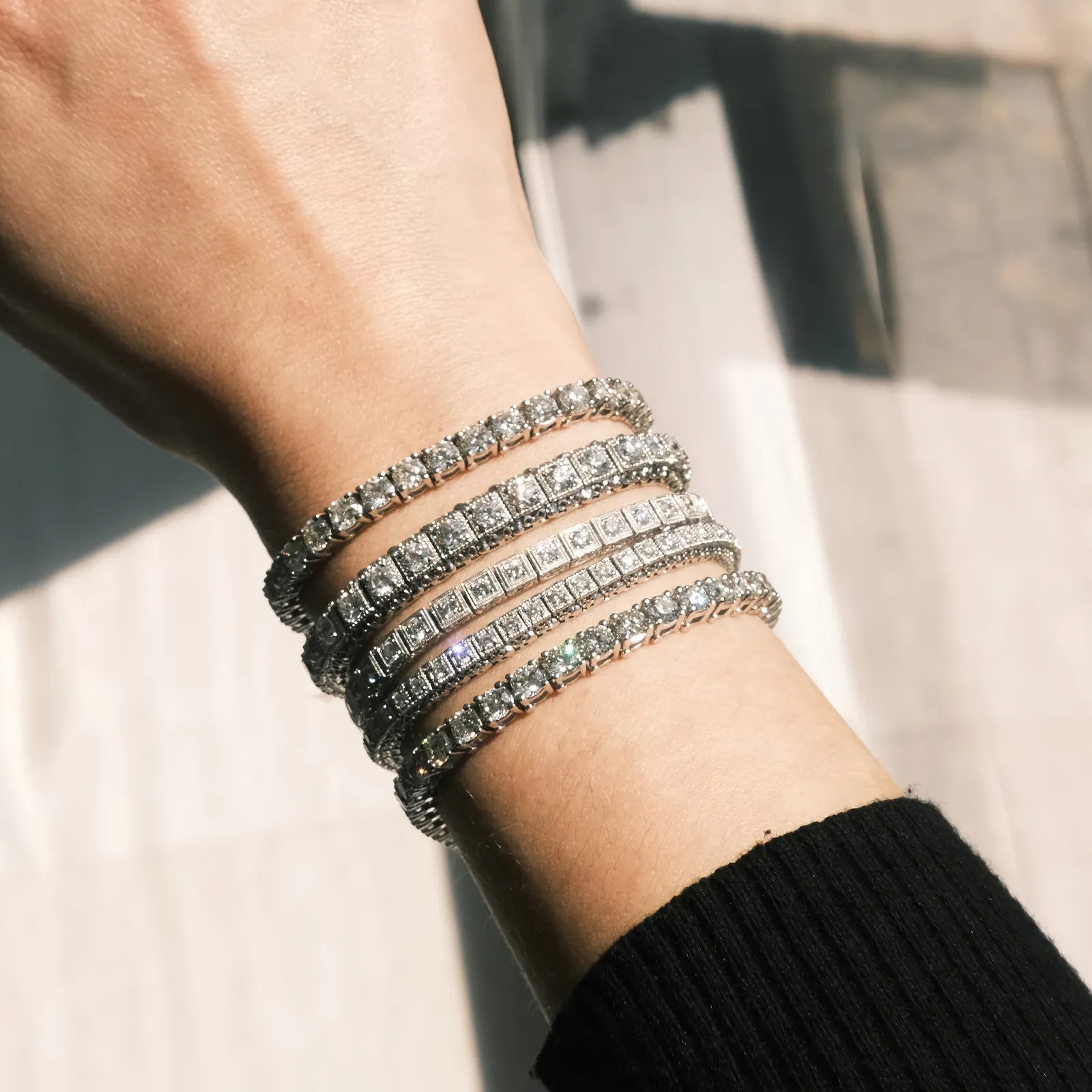 A wrist adorned with multiple sparkling diamond bracelets in sunlight.