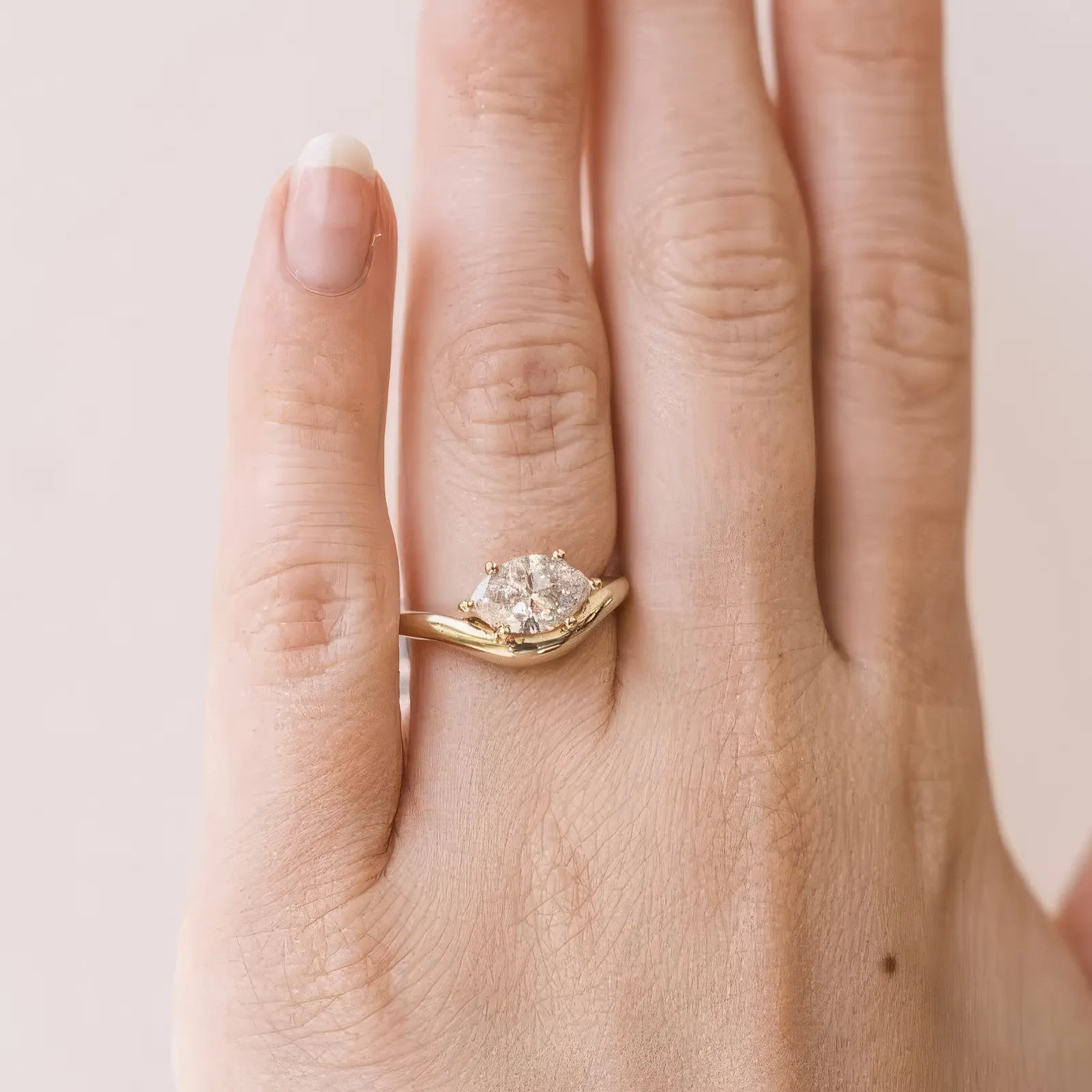A hand wearing a gold ring with a large diamond on the ring finger.