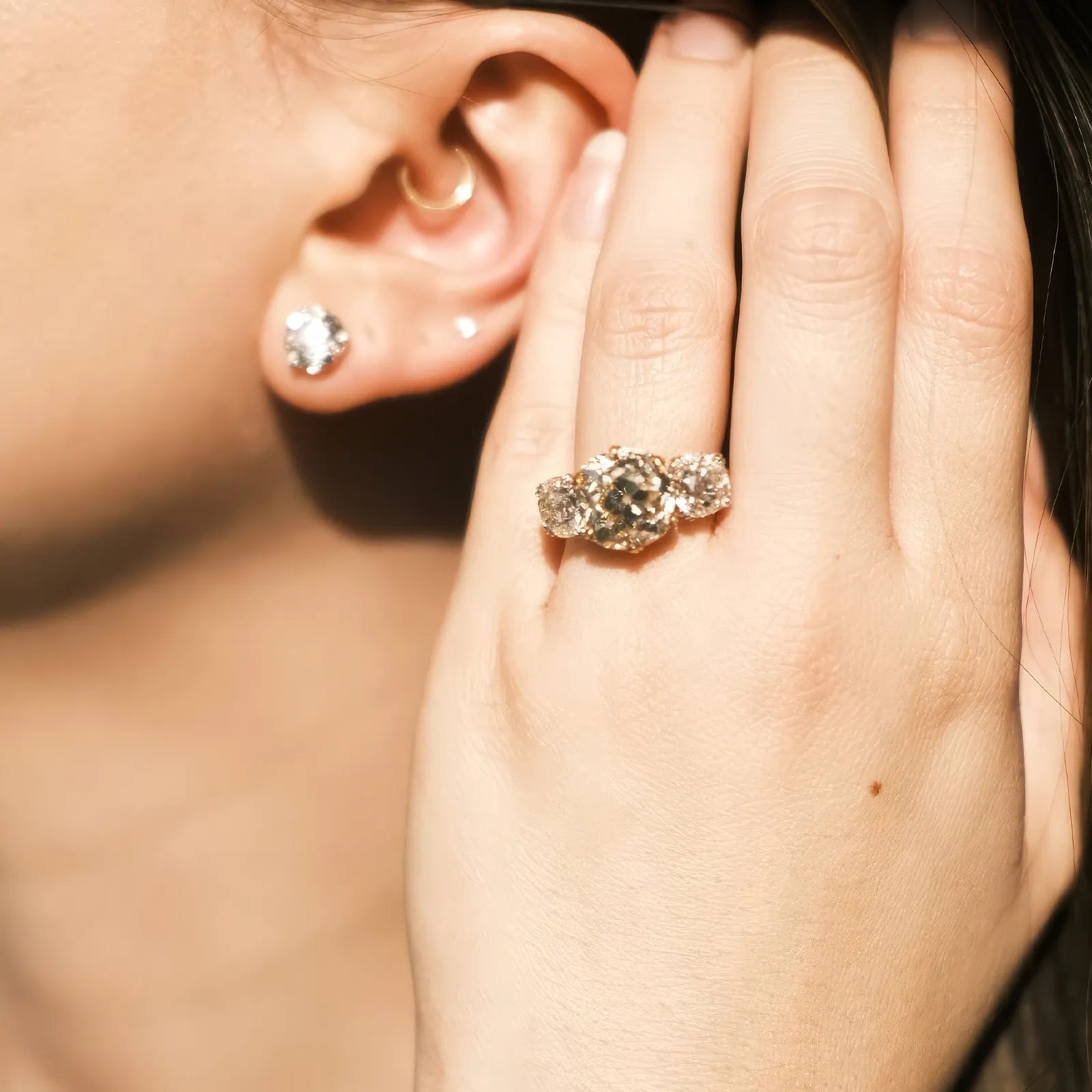 A person wearing a sparkling diamond ring and stud earring, hand near the ear.