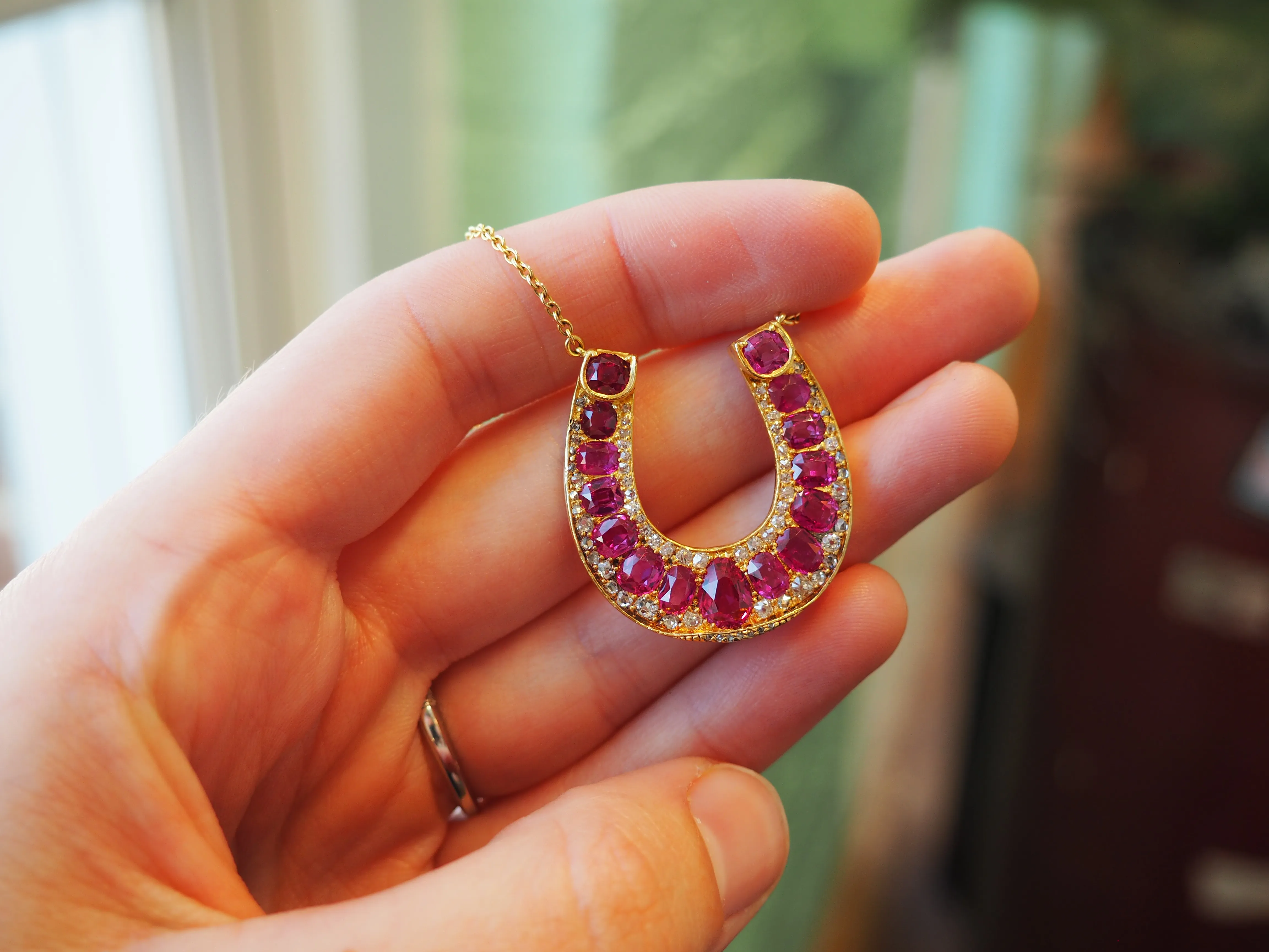 A close-up of an ear wearing a gold earring with a green gemstone and diamond accents.