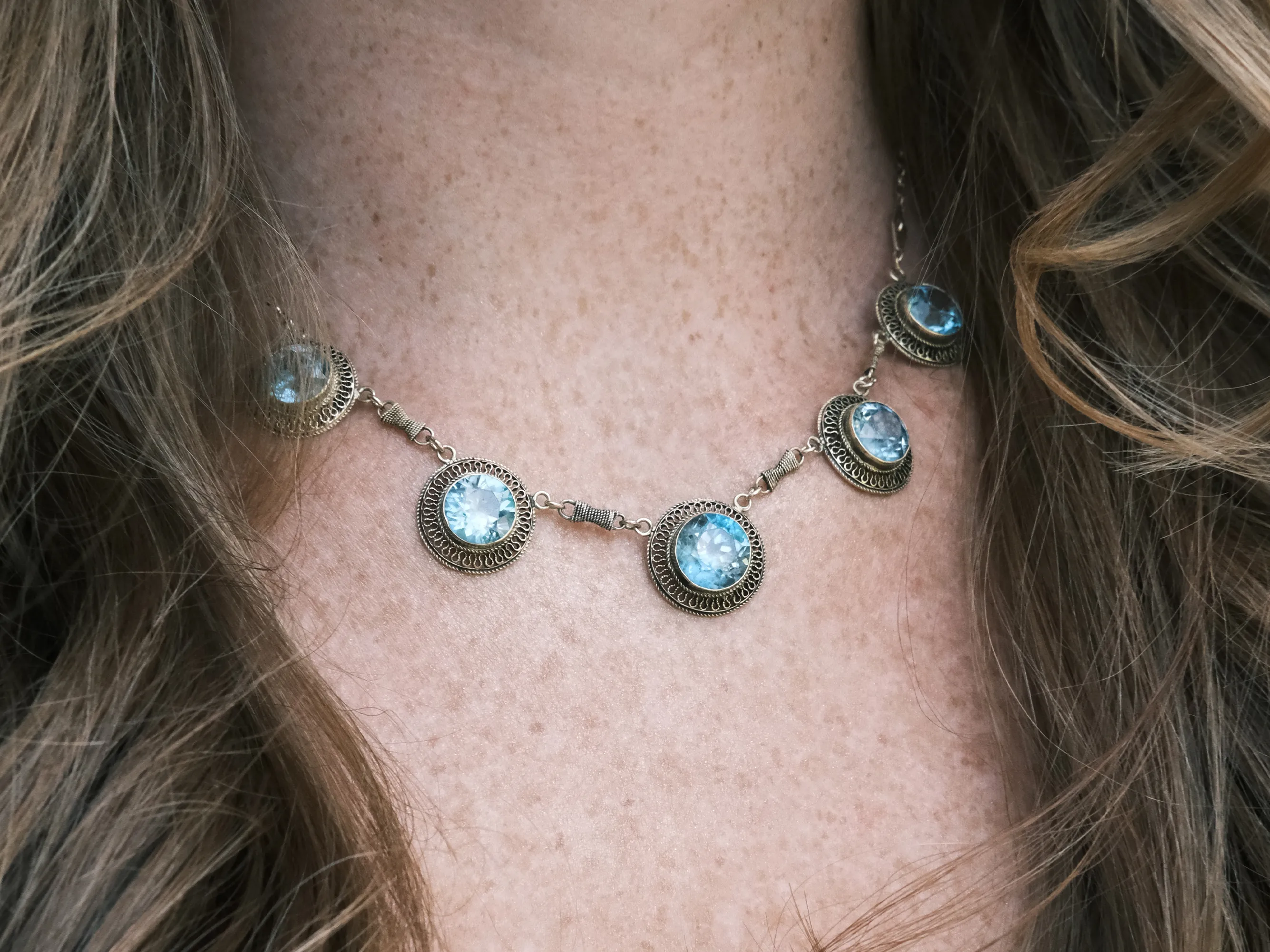 A necklace with round blue gemstones set in ornate silver settings on a person's neck.