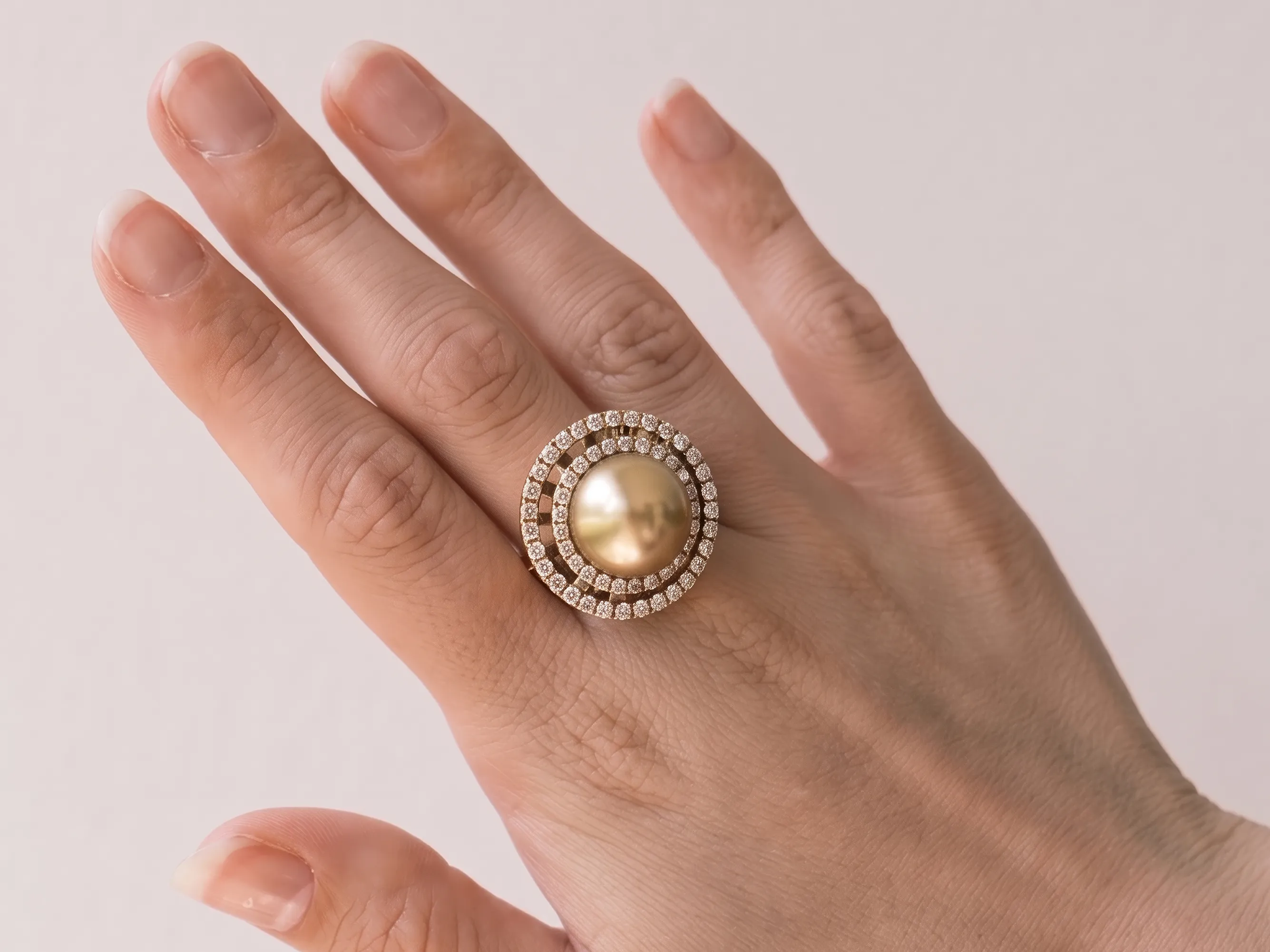 Hand wearing a large gold pearl ring with diamond accents on a light background.