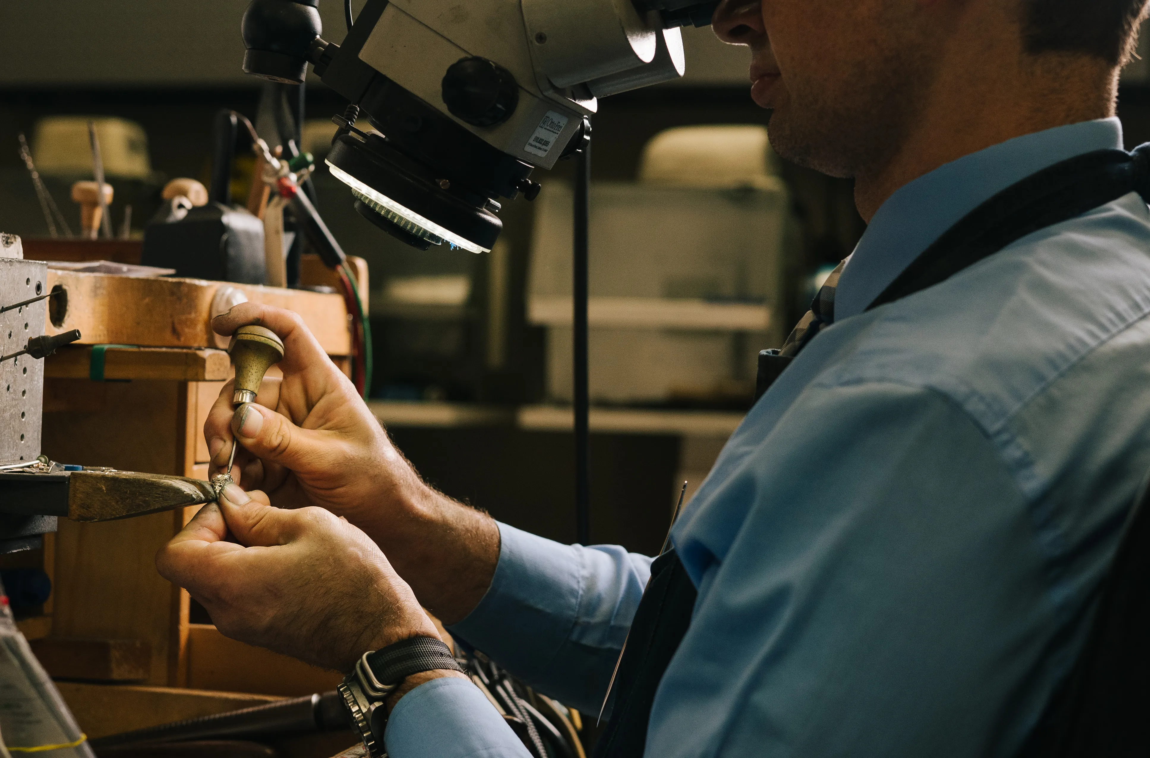 A jeweler polishing a ring on a mandrel at the bench