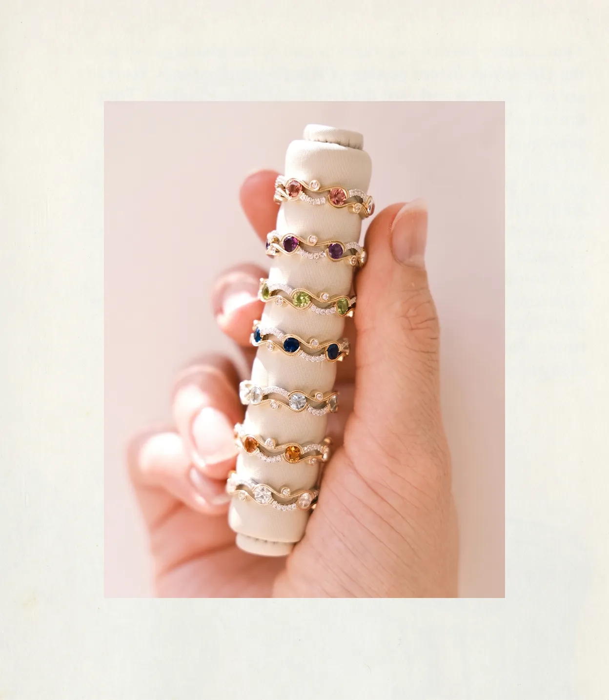 Hand holding a display of colorful gemstone rings on a padded holder.