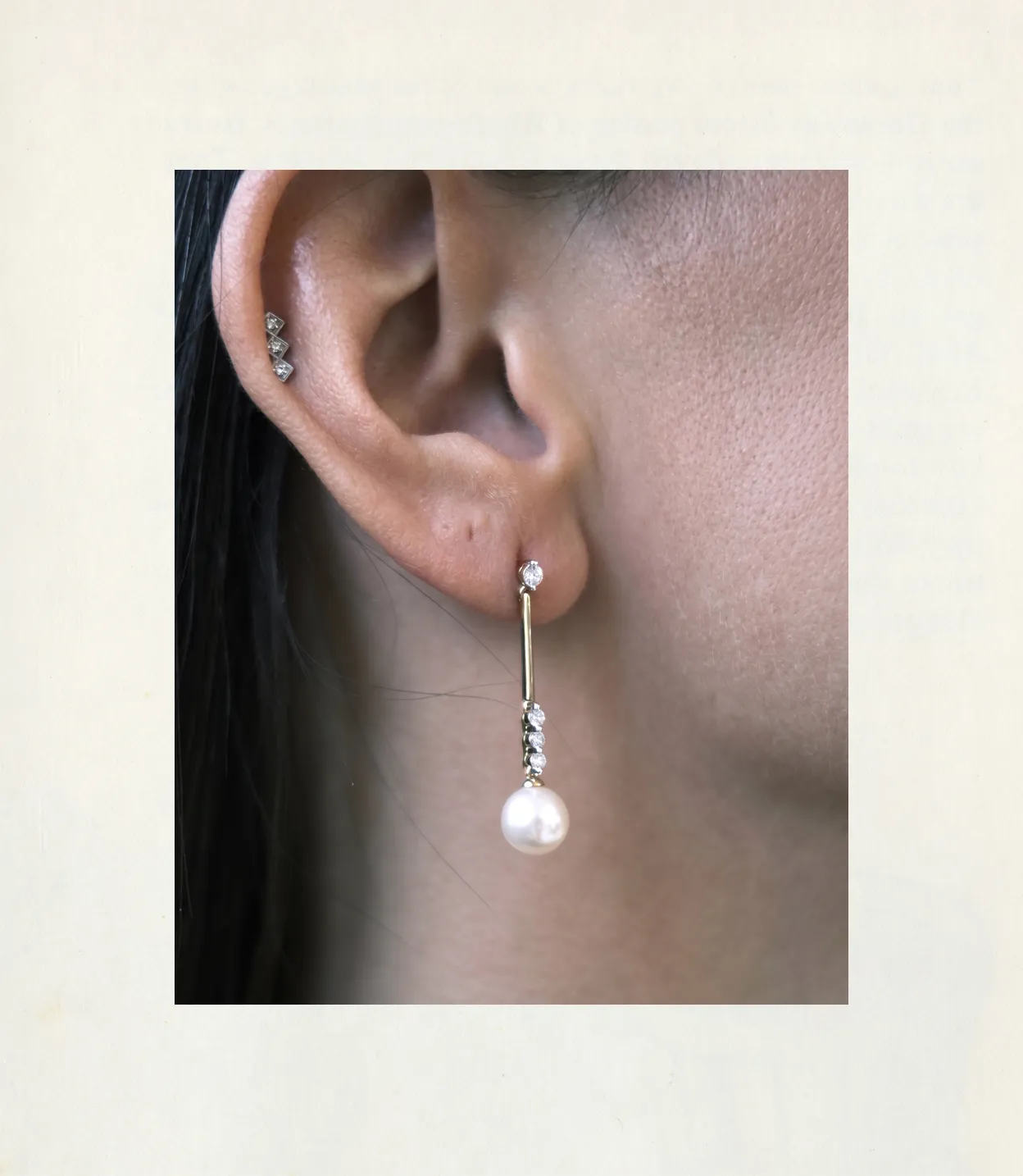 Close-up of an ear wearing a pearl drop earring with diamond accents and additional small diamond studs.