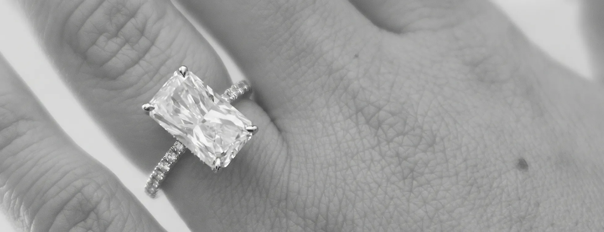 A hand wearing a large rectangular diamond ring with a diamond band.
