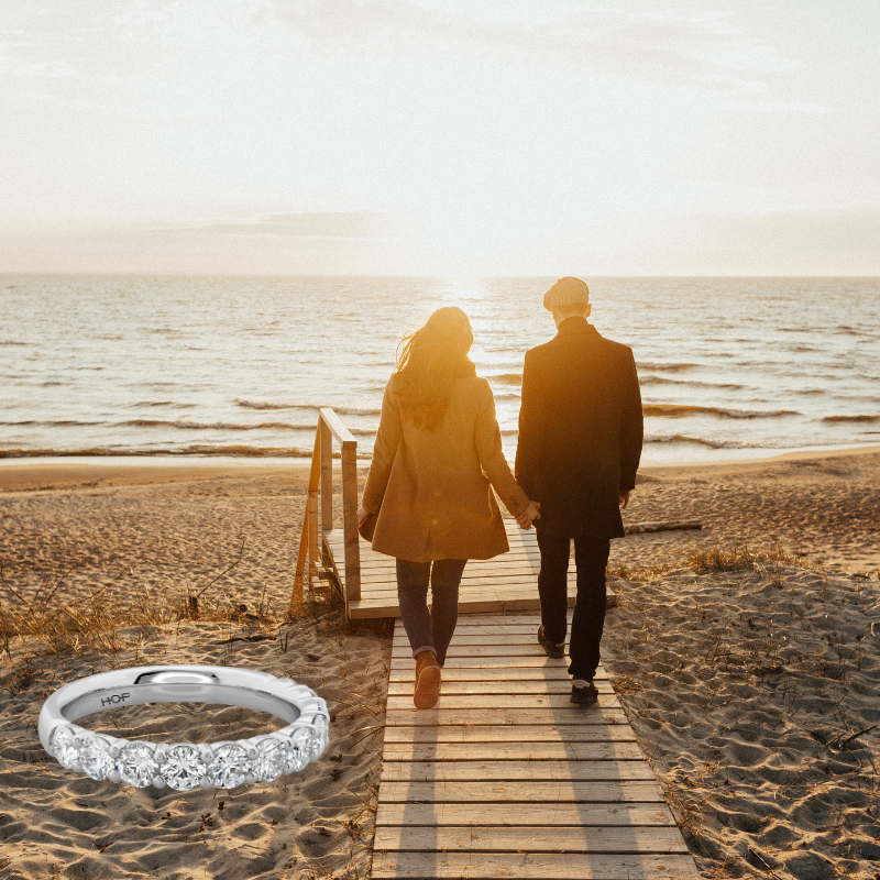 Happy couple holding hands at the beach, with a wedding ring displayed