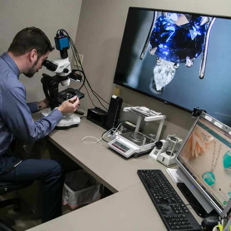 Jeweler inspecting jewelry through a microscope with TV that displays the output of the microscope