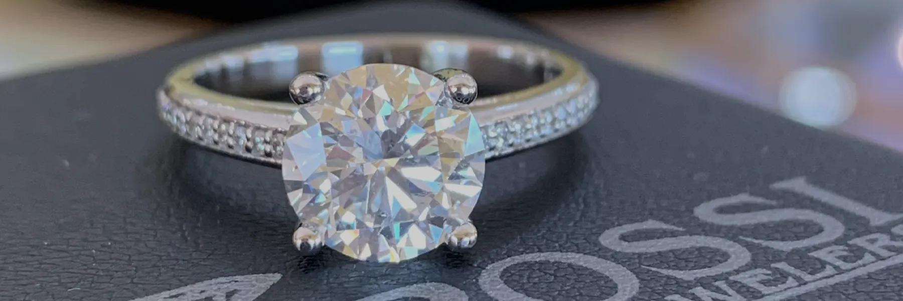 Stunning engagement ring with a large round diamond on a delicate band, displayed on a black surface. Click to view custom jewel