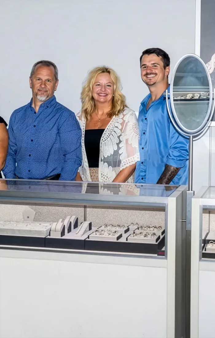 Five smiling staff members of Premier Diamond Center stand in front of jewelry displays. Click to make an appointment.