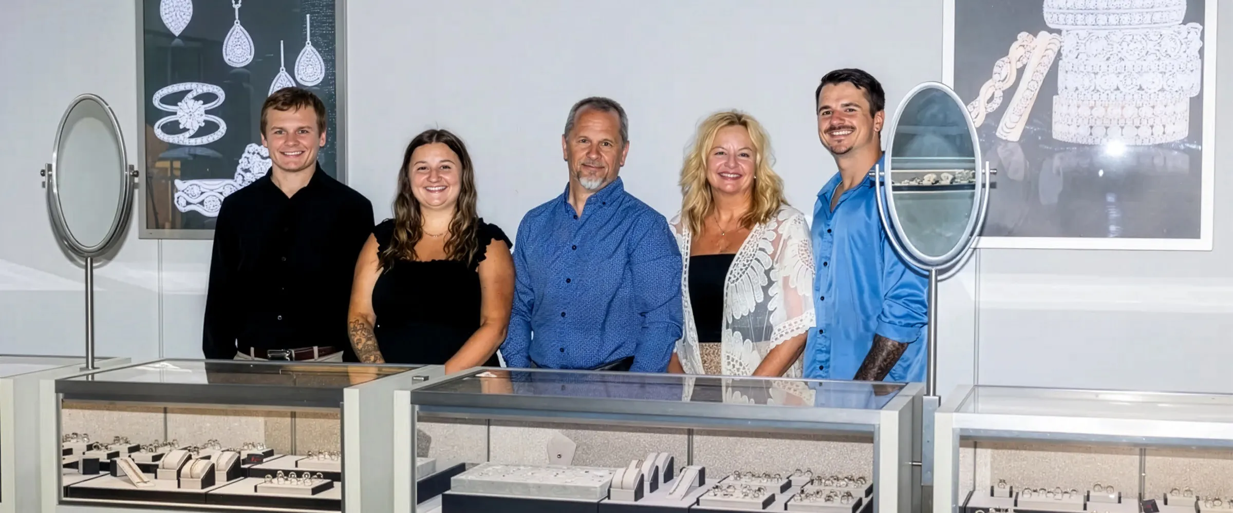 Five smiling staff members of Premier Diamond Center stand in front of jewelry displays. Click to make an appointment.