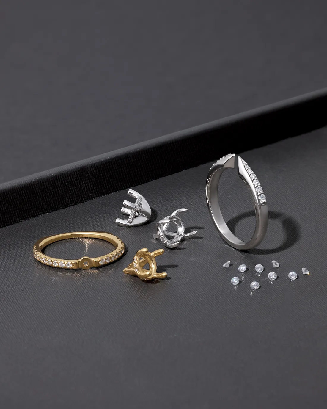 Various elegant rings and earrings displayed on a dark surface, showcasing diamond settings. Click to Shop Now.