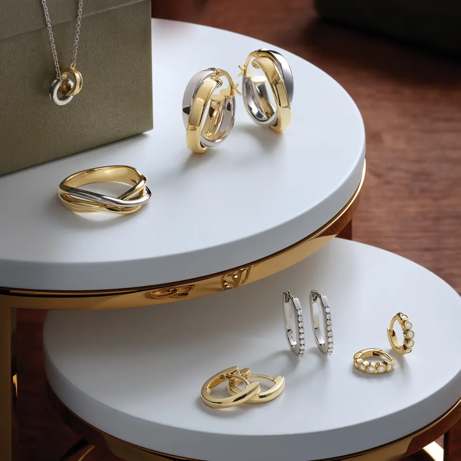 Elegant gold and silver earrings displayed on a stylish table, with a necklace in the background. Shop at Premier Diamond Center