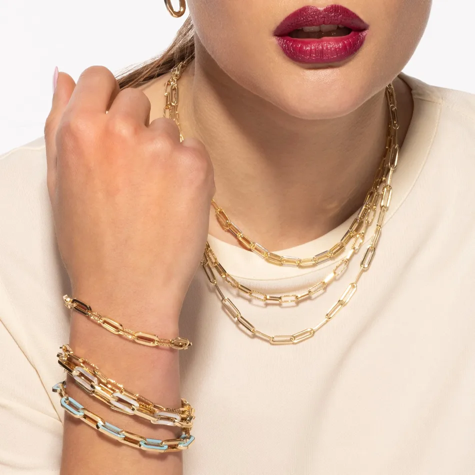 Model showcasing layered gold chain necklaces and bracelets, featuring a bold lip color. 