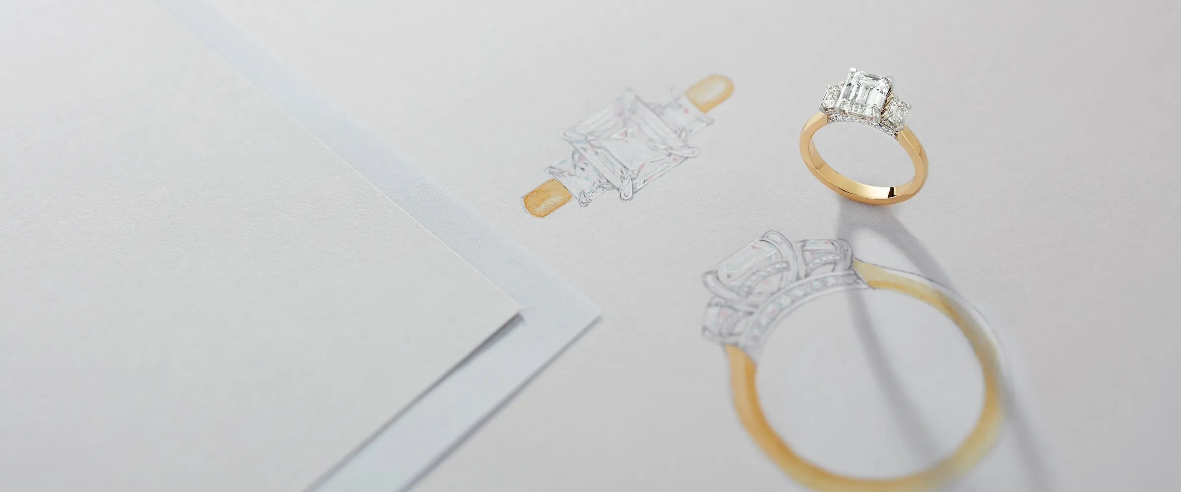 Engagement ring sketch and actual ring on paper, showcasing custom jewelry design by Premier Diamond Center. Start a project!
