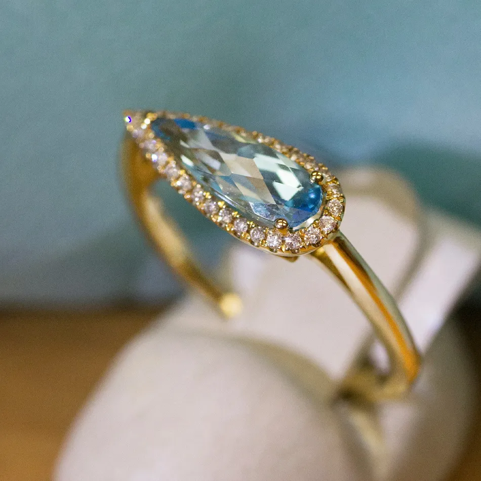 Elegant gold ring with a pear-shaped blue gemstone and diamond accents.