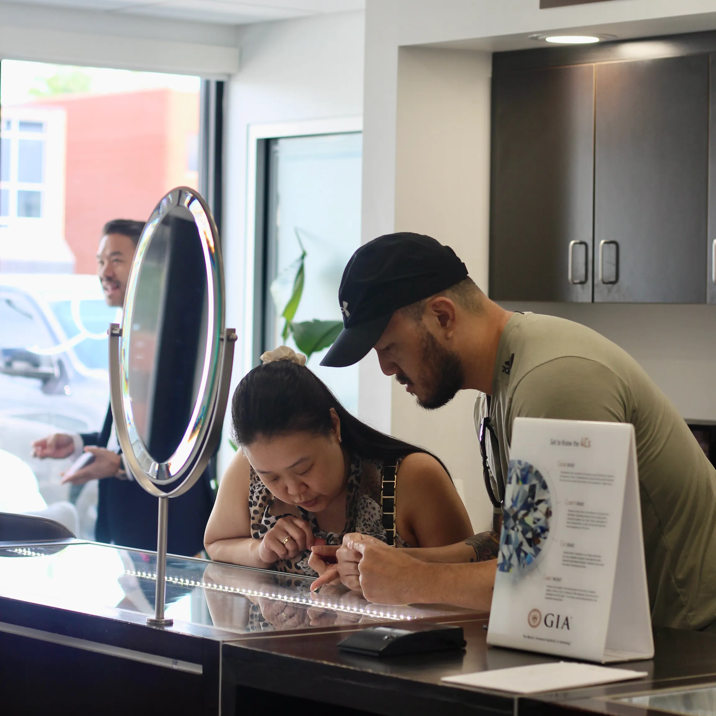 A woman examines a ring with a man at Quest Fine Jewelers, while another man smiles in the background.